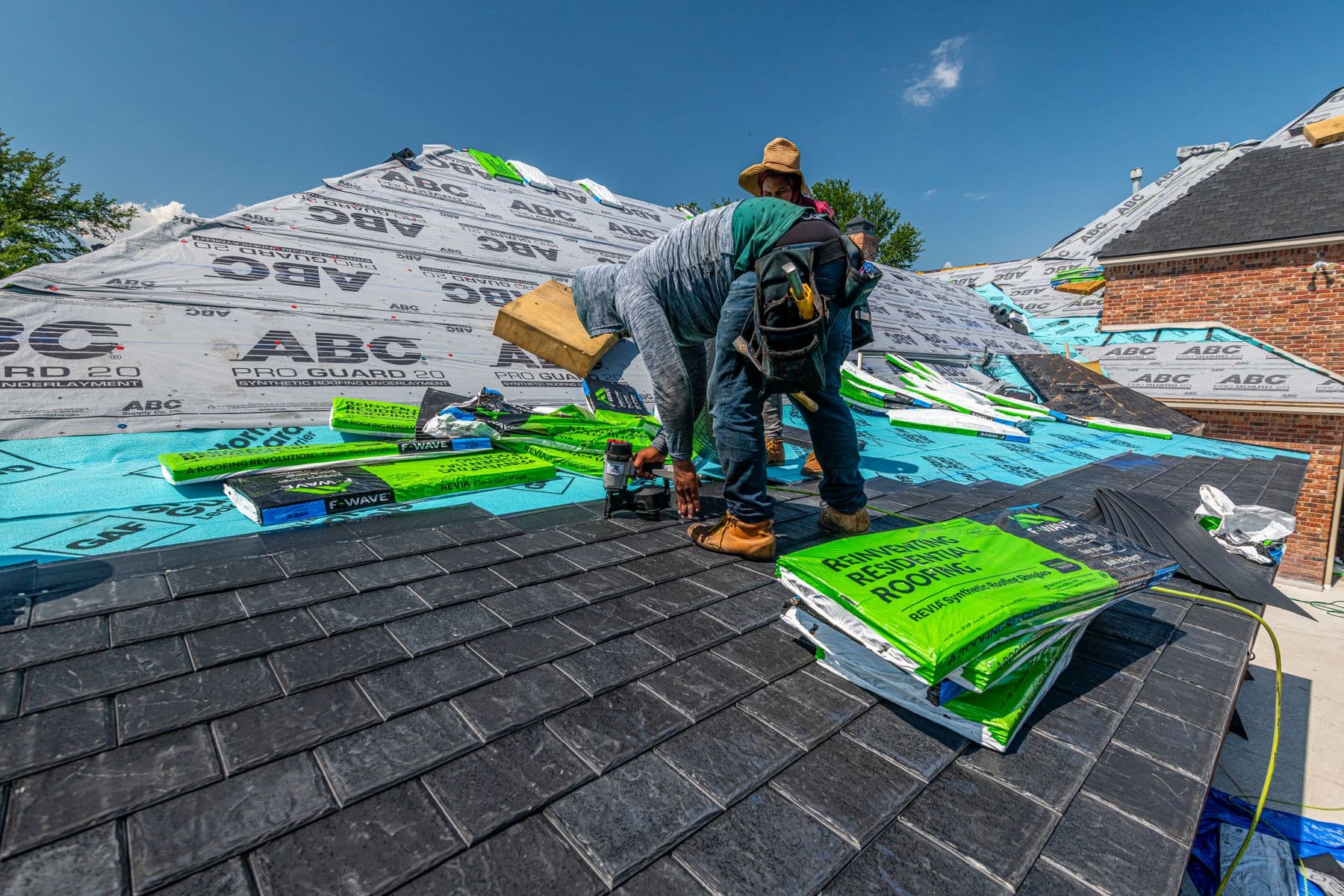 Crew installing asphalt shingles over underlayment on a residential roof